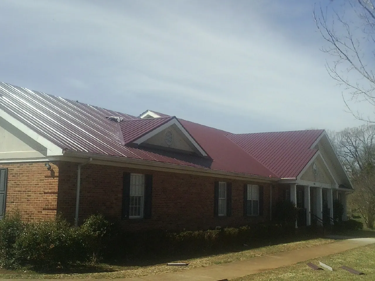 Red metal roof with gabled entries on a long brick building, from a Hail Damage Roof Repair job in Almo