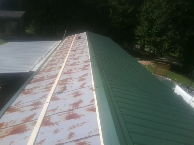 Old rusted panels beside newly installed green metal roofing — Wind Damage Roof Repair by Roofing Brothers in Almo