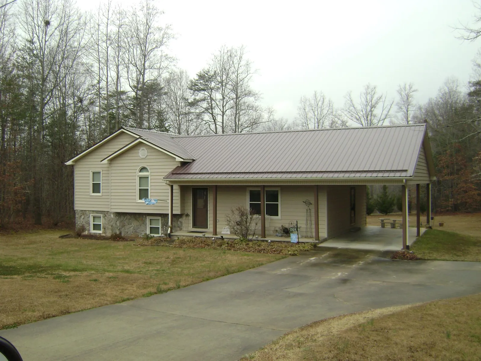 Brown metal roof on a tan split level home with an attached carport in Almo