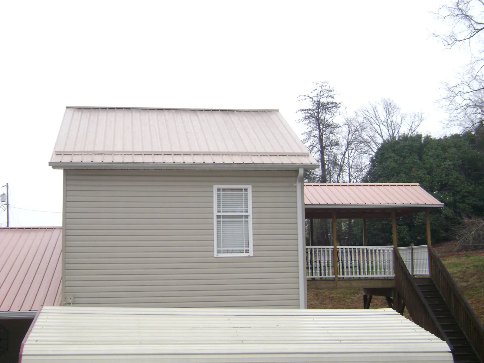 Tan metal roofs on a two story addition and attached porch, from a Roof Replacement job in Almo